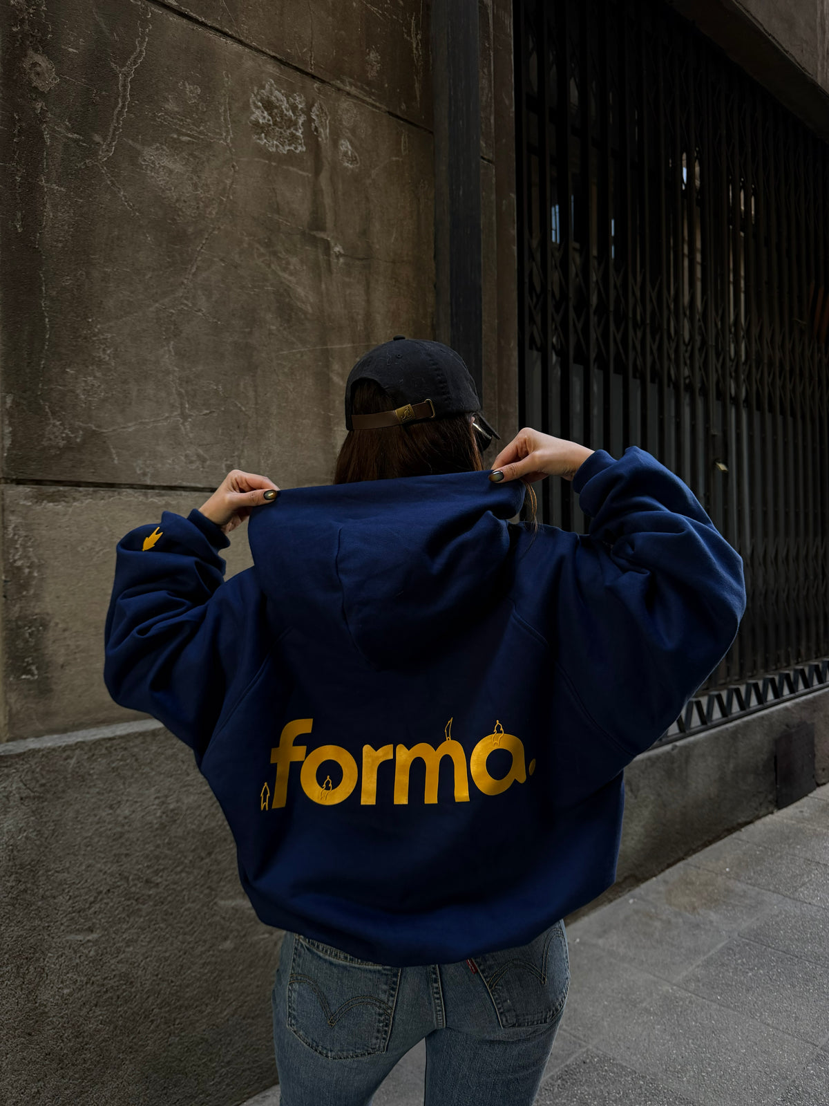 Persona con hoodie azul FORMA en la calle, de espalda con logo amarillo